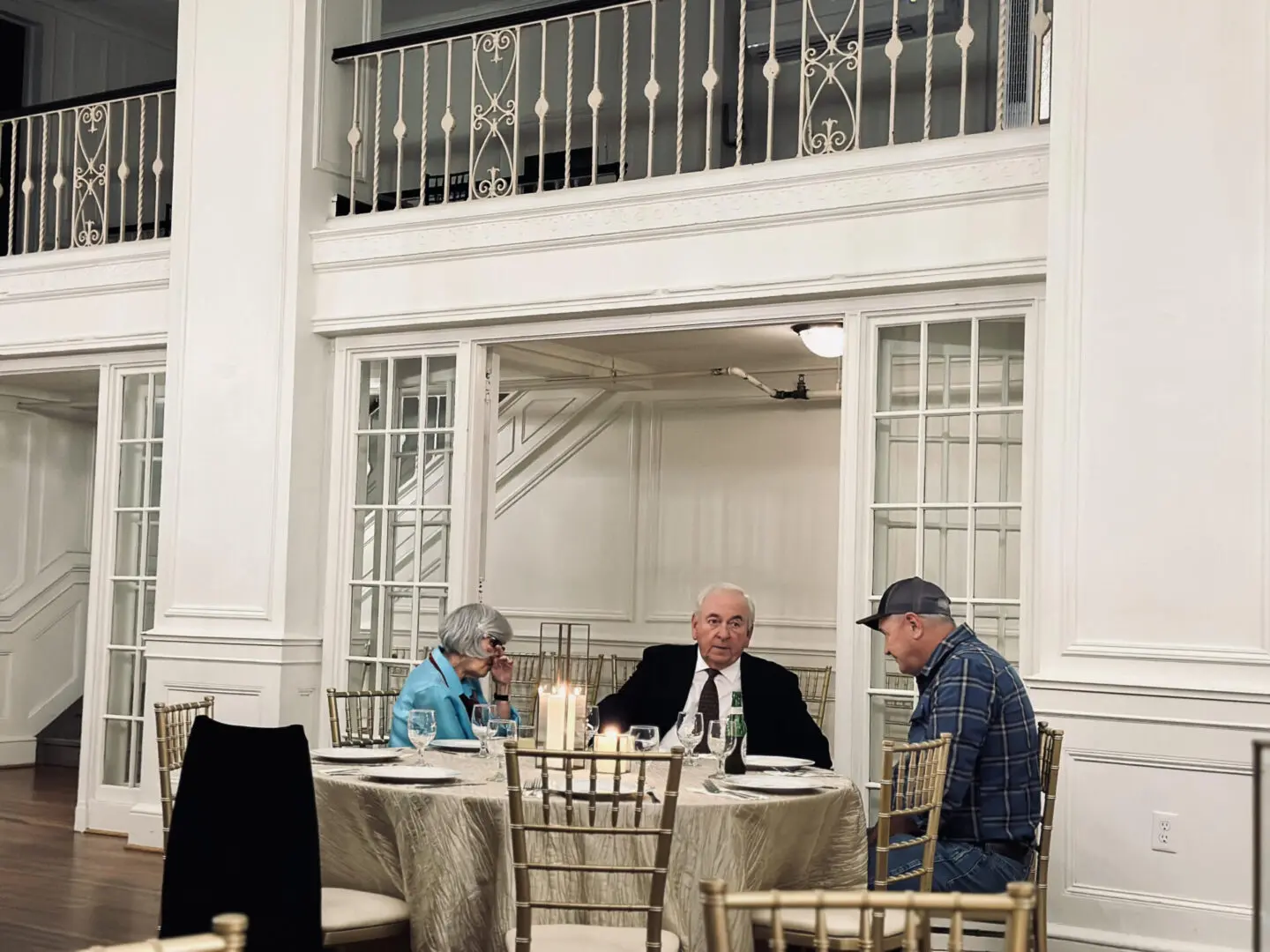 Three people sitting at a table in front of two windows.